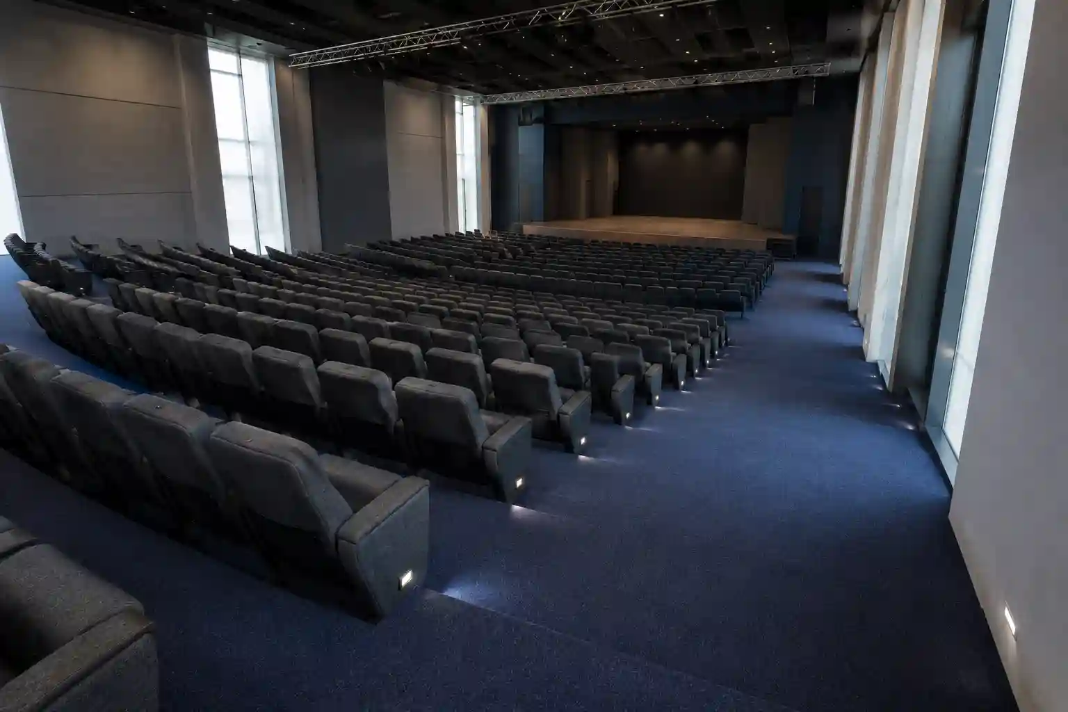 Auditorio universitario en Puebla con alfombra de rollo azul de alto desempeño instalada de pared a pared en pasillos y gradas, butacas tapizadas en gris y escenario de madera al fondo.