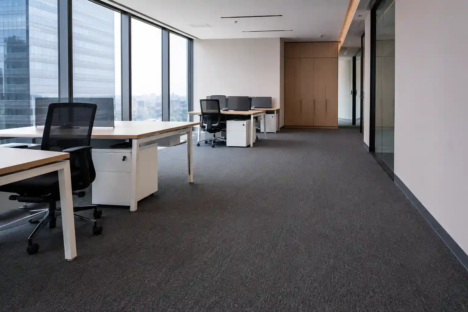 Oficina corporativa en Angelópolis, Puebla, con alfombra de rollo gris de alto tránsito instalada de pared a pared, escritorios de madera clara con sillas ejecutivas negras y ventanales con vista panorámica de la ciudad.